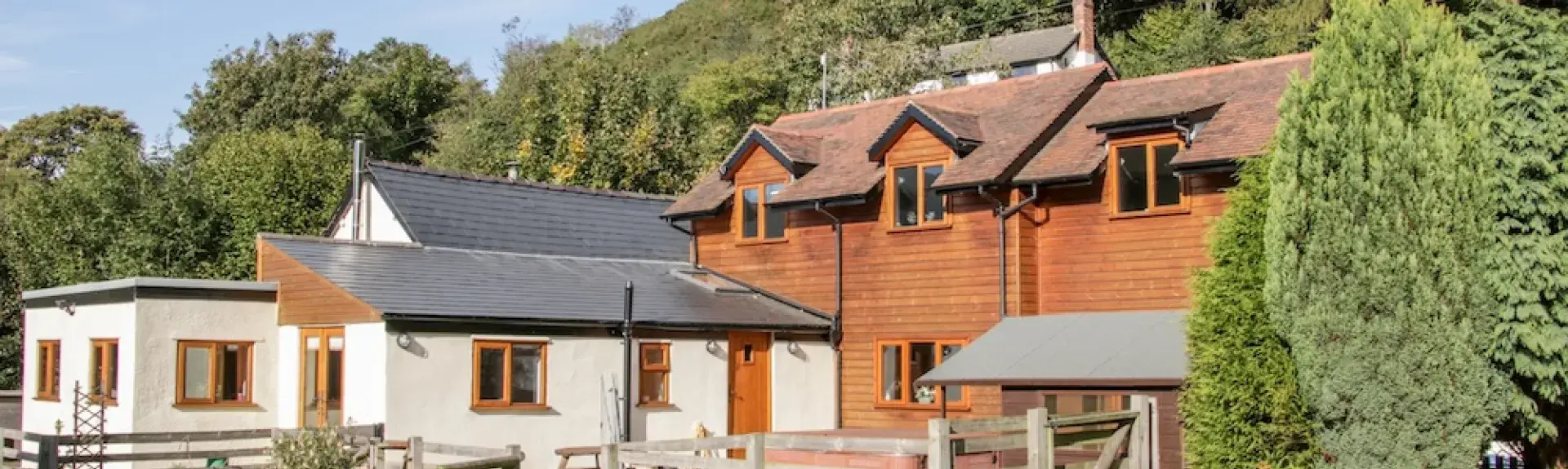 A wooden-clad Shropshire holiday home overlooks a lawn backed by trees.