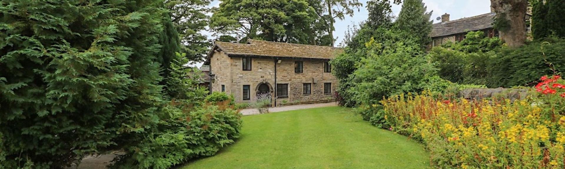 A Somerset stone barn conversion overlooks a large lawn lined by flower beds and shrubs.