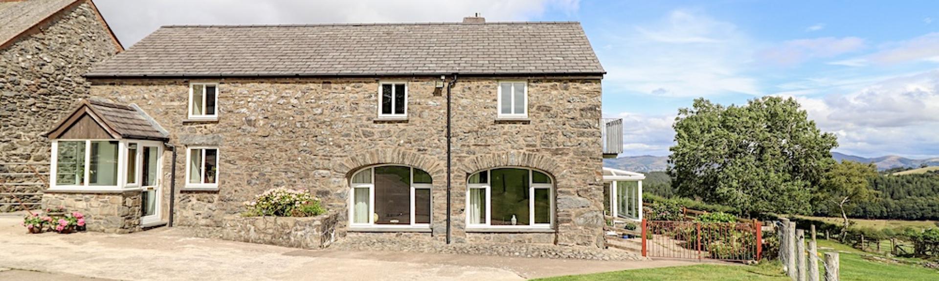 A 2-storey barn conversion overlooks a paved courtyard and open countryside in North Wales.