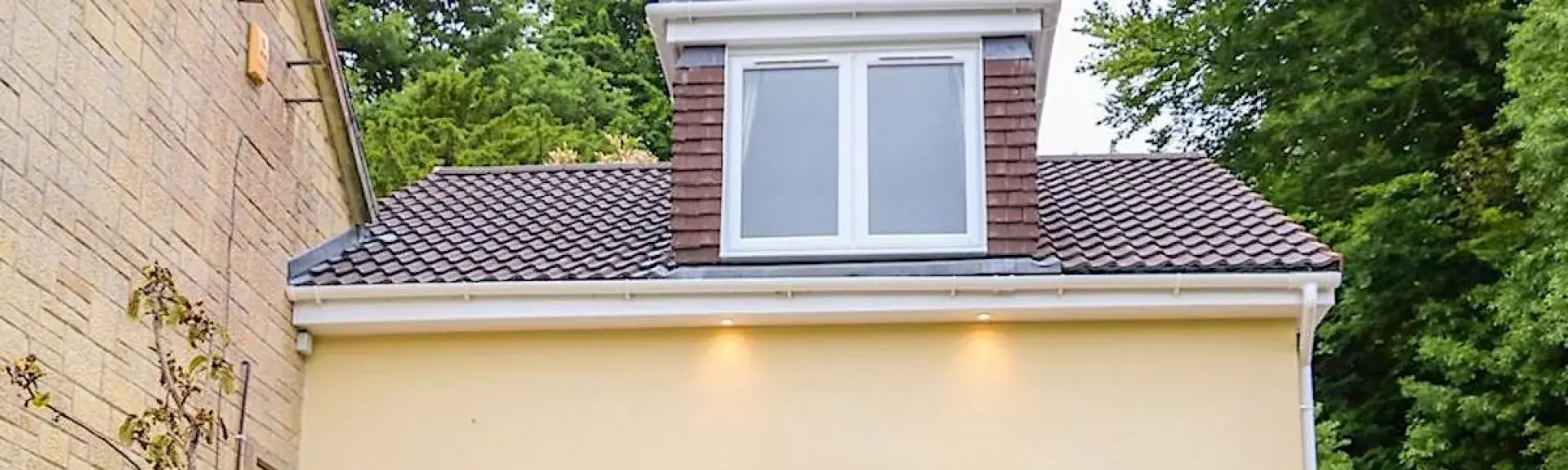 A semi-detached chalet bungalow with French Windows onto a patio with steps down to a flower-lined lawn.