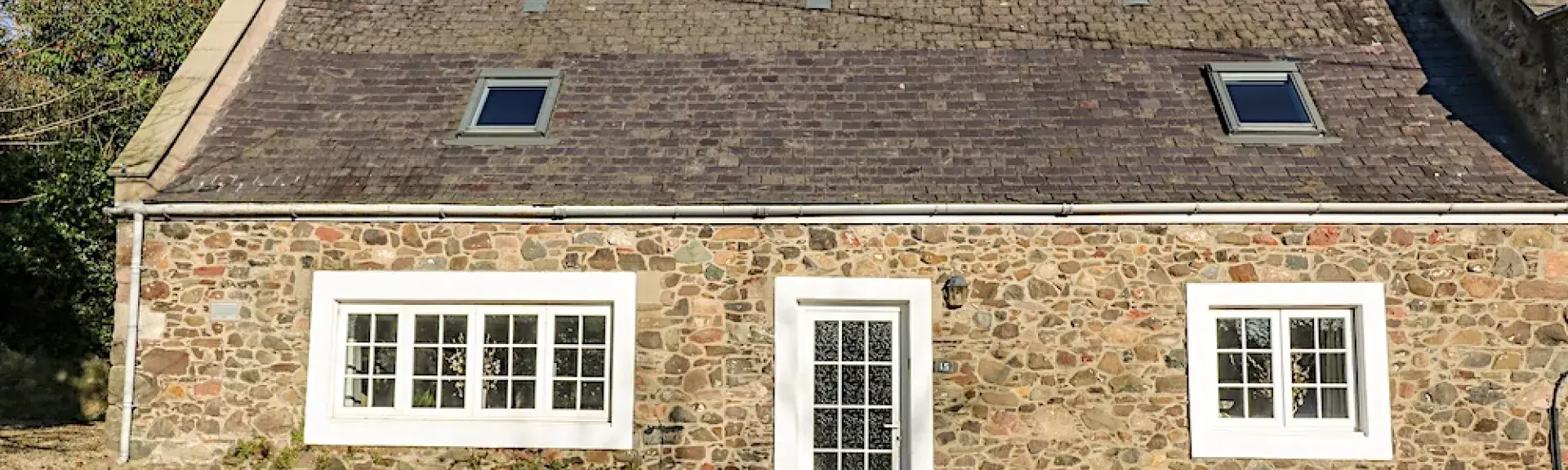 Exterior of a stone-built single storey cottage with a slate roof overlooking an empty cobbled street.