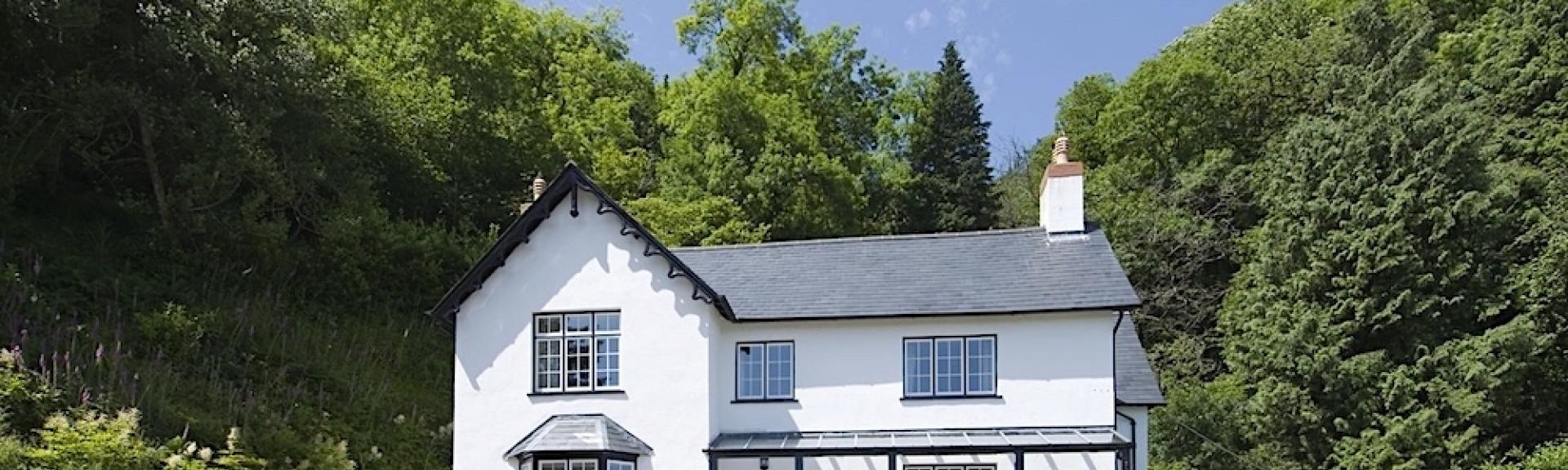A 2-storey Exmoor holiday cottage stands in front of a bank of mature trees.