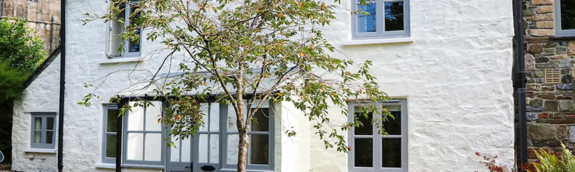 Exterior of a two-storey Devon holiday cottage with rendered walls and a slate roof overlooking a lawn.