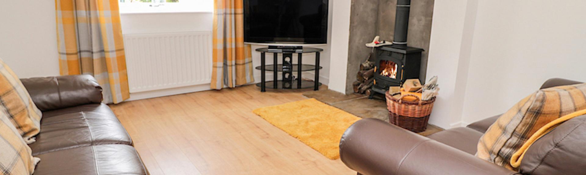 A spacious wooden floored lounge with twin sofas, TV and a woodburner.
