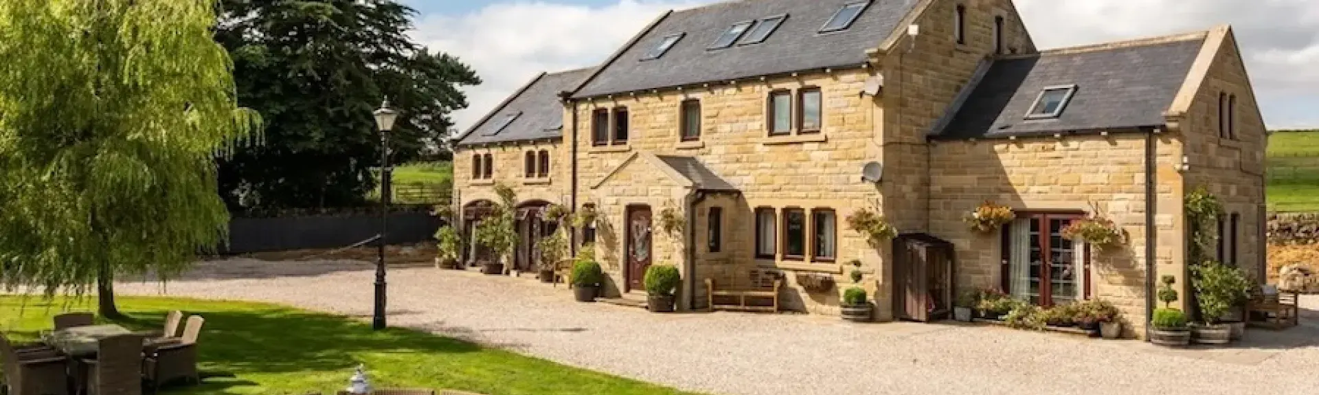 Exterior of a large stone-built Dales farmhouse with 2 wings, a large lawn and fields all around it.