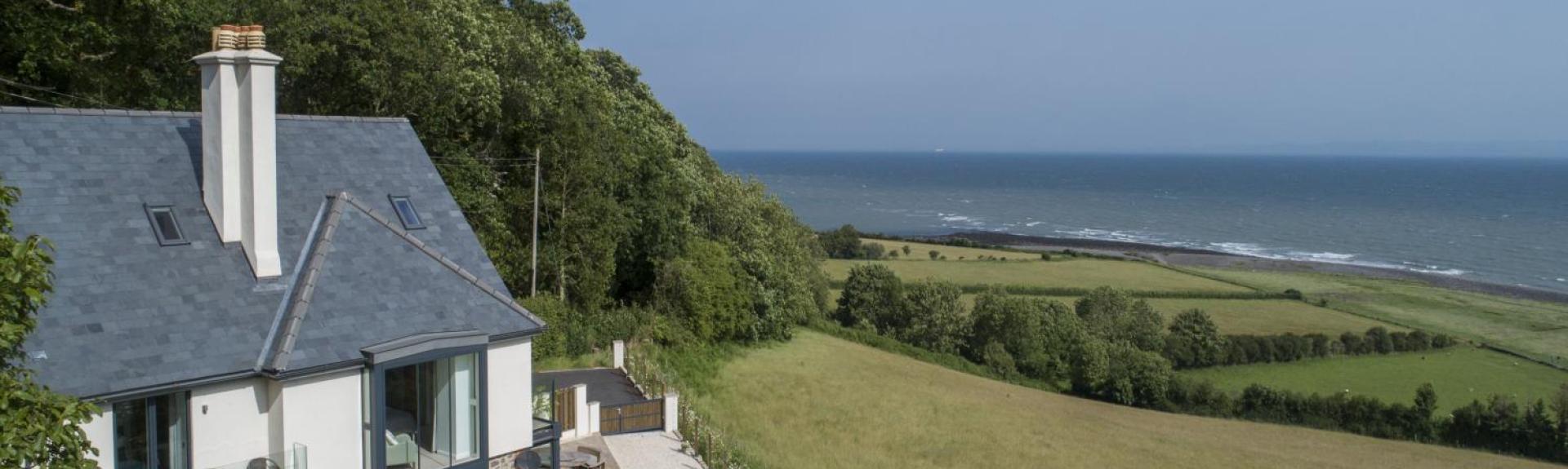 A large contemporary holiday cottage overlooks fields dipping down to a beach and ocean views.