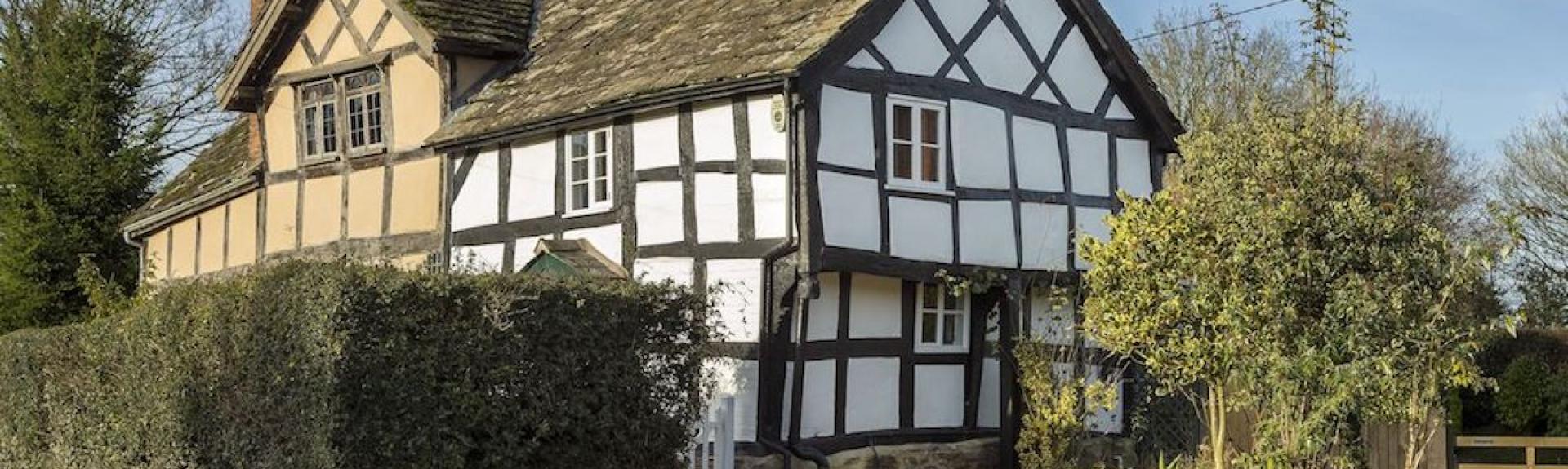 A half-timbered Tudor cottage  in Leominster overlooks a shingle parking space and shrub-filled garden.