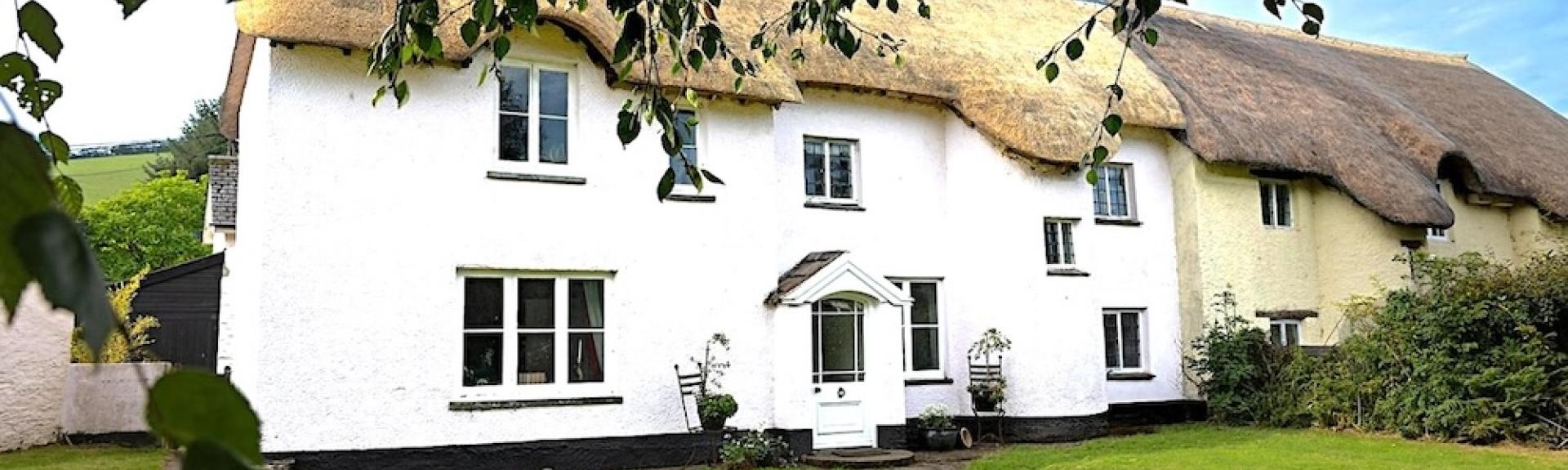 Exterior of a thatched Exmoor cottage overlooking a large lawn.