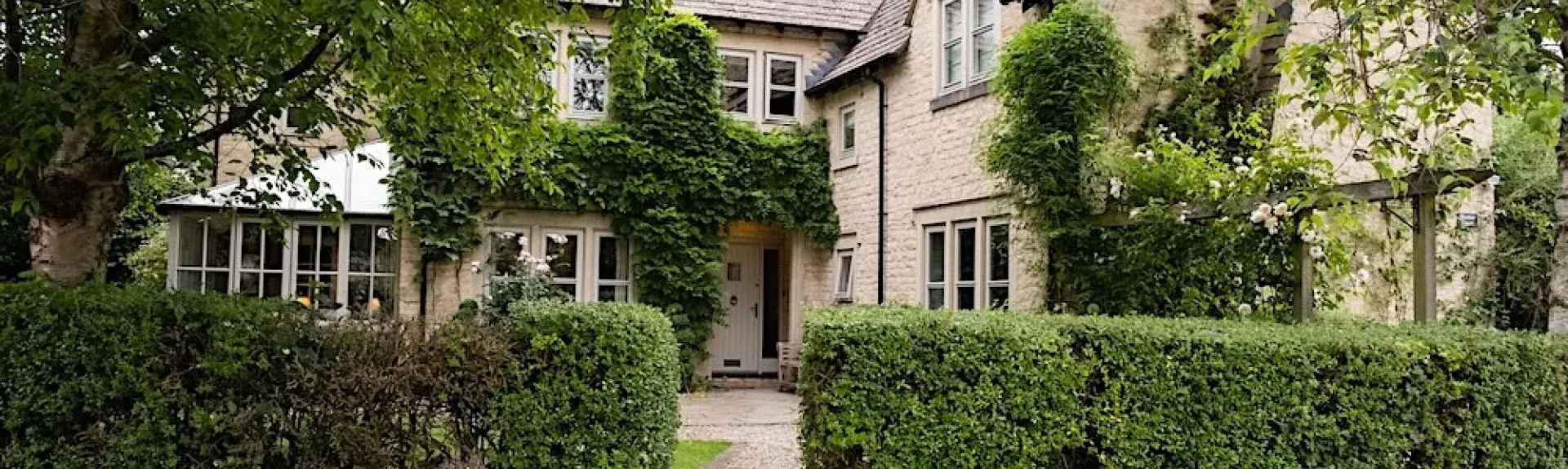 Behind a hedge is a large L-shaped contemporary cottage with a conservatory.