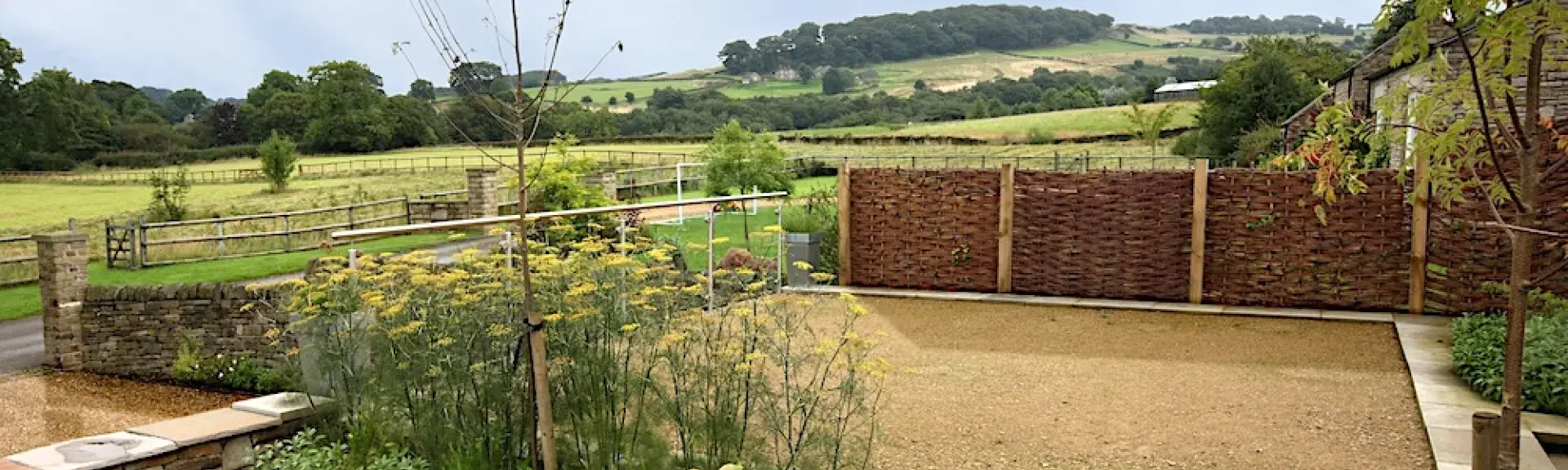 A cottage garden with rural views of hills and open countryside beyond a hedge.