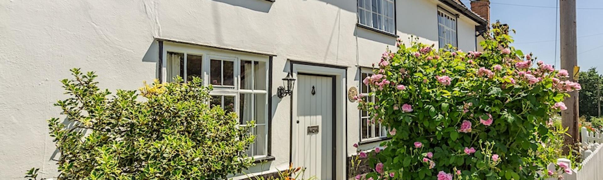 A double-fronted Sussex cottage with a flower-filled front garden behind a low picket fence.
