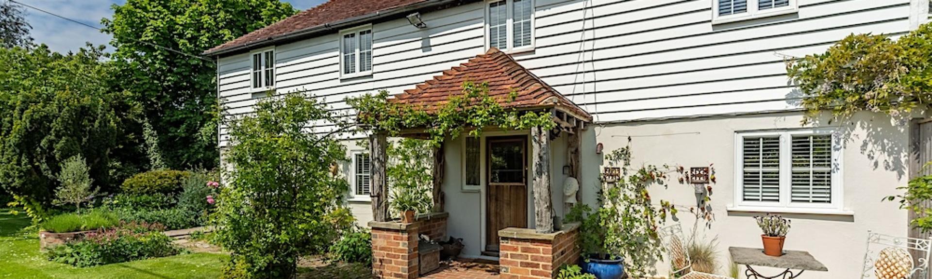 Exterior of a weather-boarded East Sussex Cottage and lawned garden.
