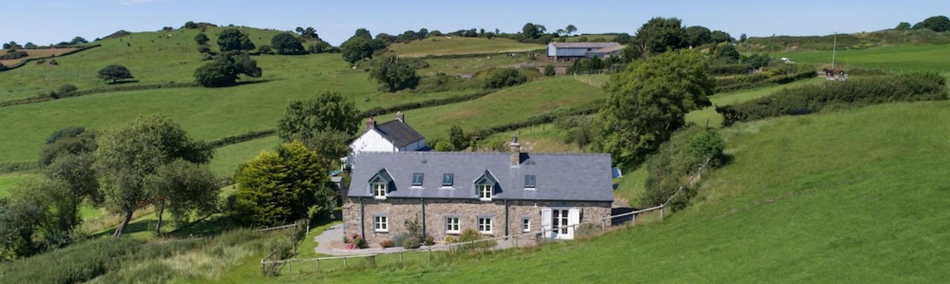 A 2-storey stone-built holiday cottage nestles in a fold a rural landscape.