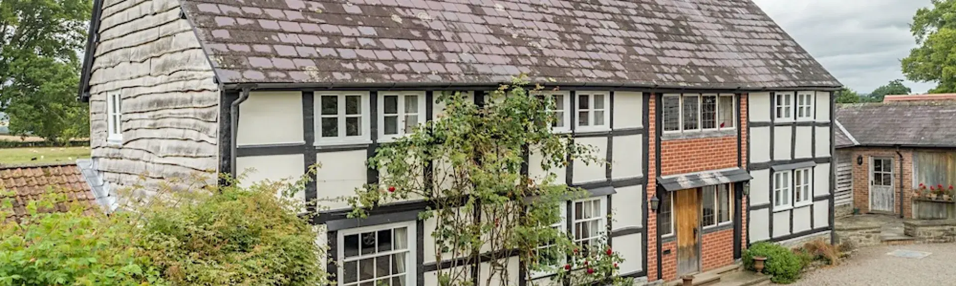 Exterior of a cross-timbered cottage overlooking a large shingle parking area.
