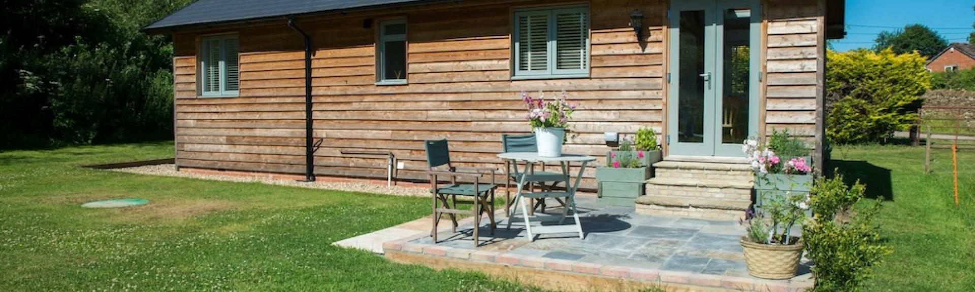 A weatherboard barn conversion with a patio having a small table and chairs.
