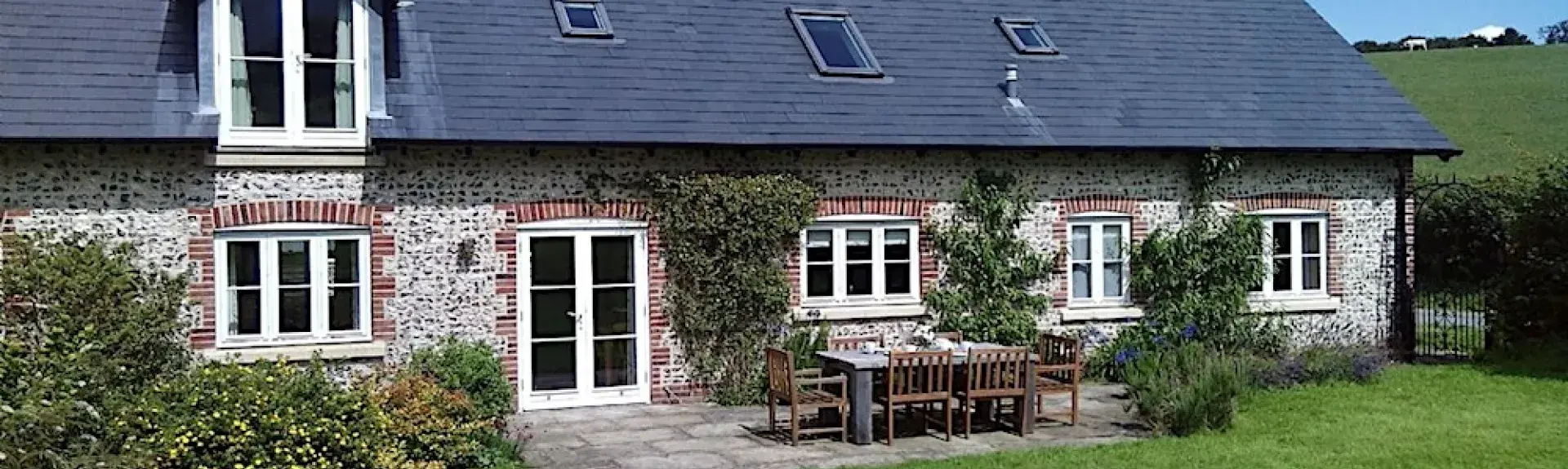 2-storey barn conversion with a patio for dining and large lawn.