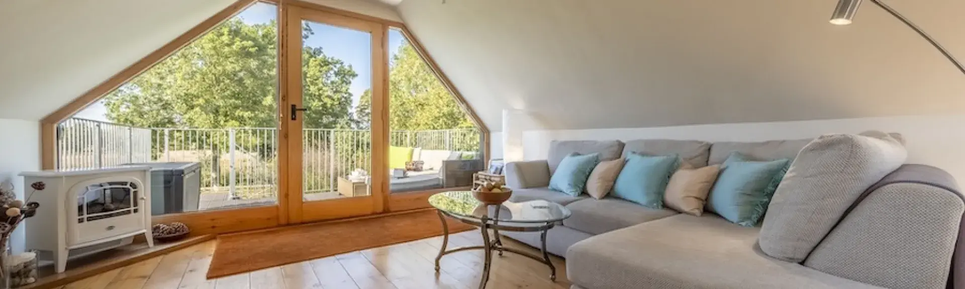 A clapper-boarded barn conversion with steps to a balcony half-hidden between trees.