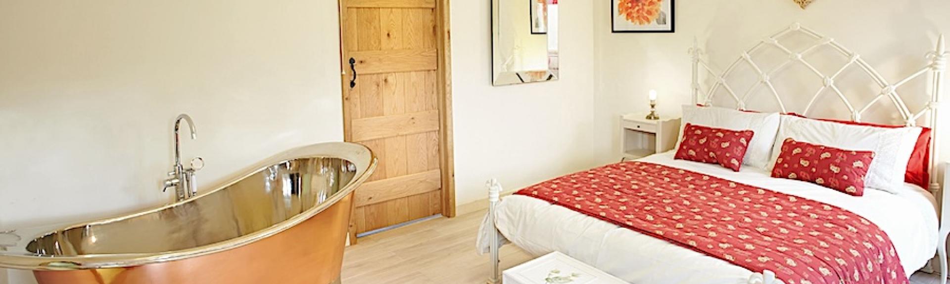 A spacious double-bedroom with a bed and deep, polished copper bath.