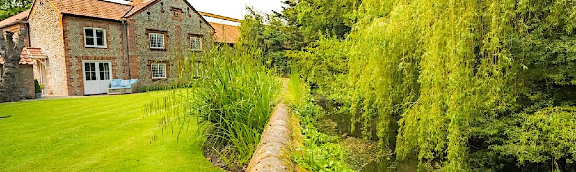 A Norfolk cottage overlooks a spacious lawn and a riverbank with willow trees.