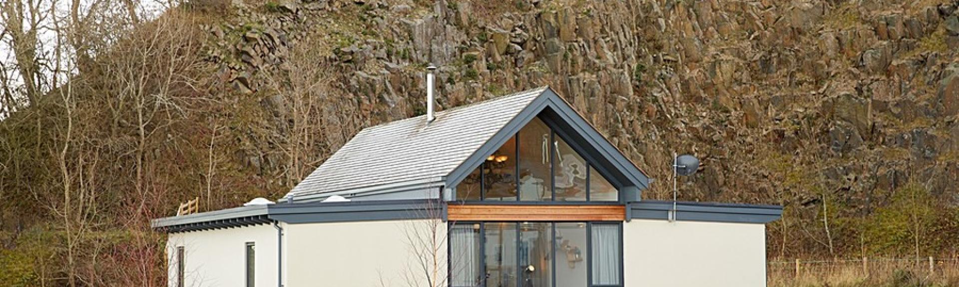 A contemporary Northumblerland holiday lodge beneath a sheer rocky hill face.