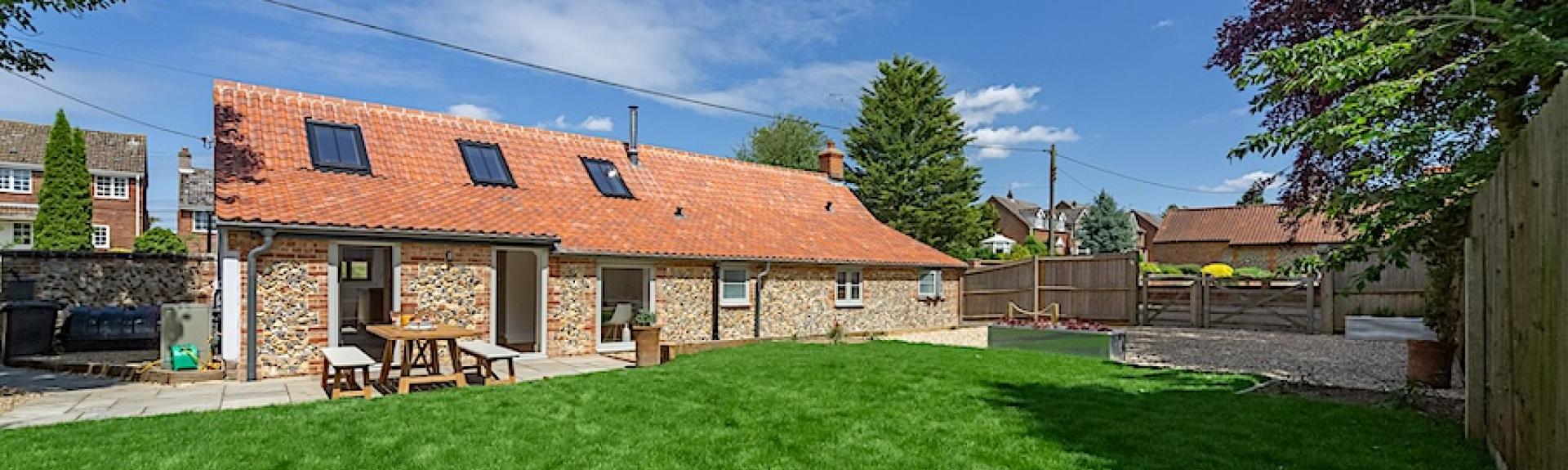 A single storey barn conversion overlooking a patio and securely-fenced lawn.