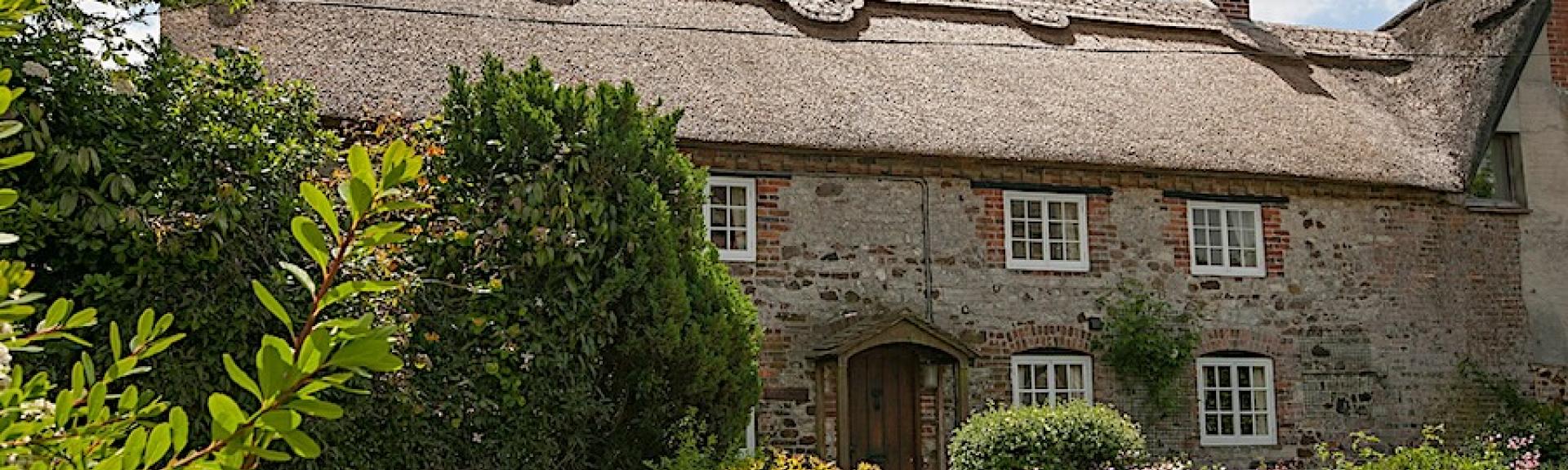 Exterior of a thatched holiday cottage in Dorset with a flower-filled garden.