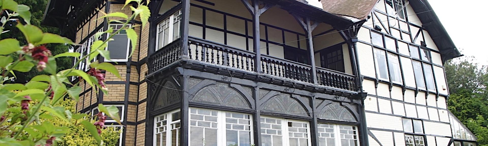 Exterior of a large mock Tudor house with 1st floor balcony.