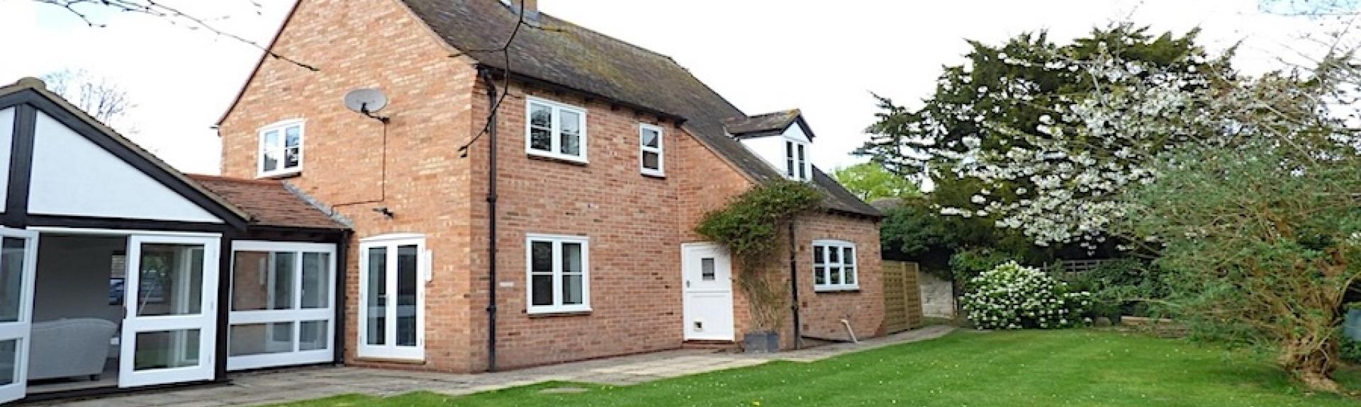 A brick-built holiday home with single storey extensions and a large, tree-lined and well-mown lawn