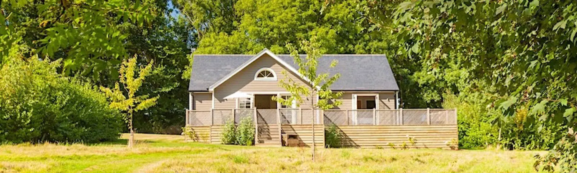 A timber eco-lodge backed by trees overlooks an open field.