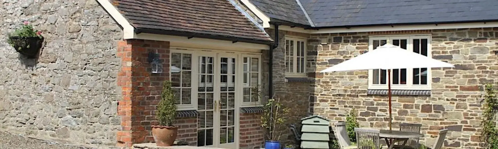 Exterior of a single-storey, stone-built cottage with a patio containing a dining table and chairs.