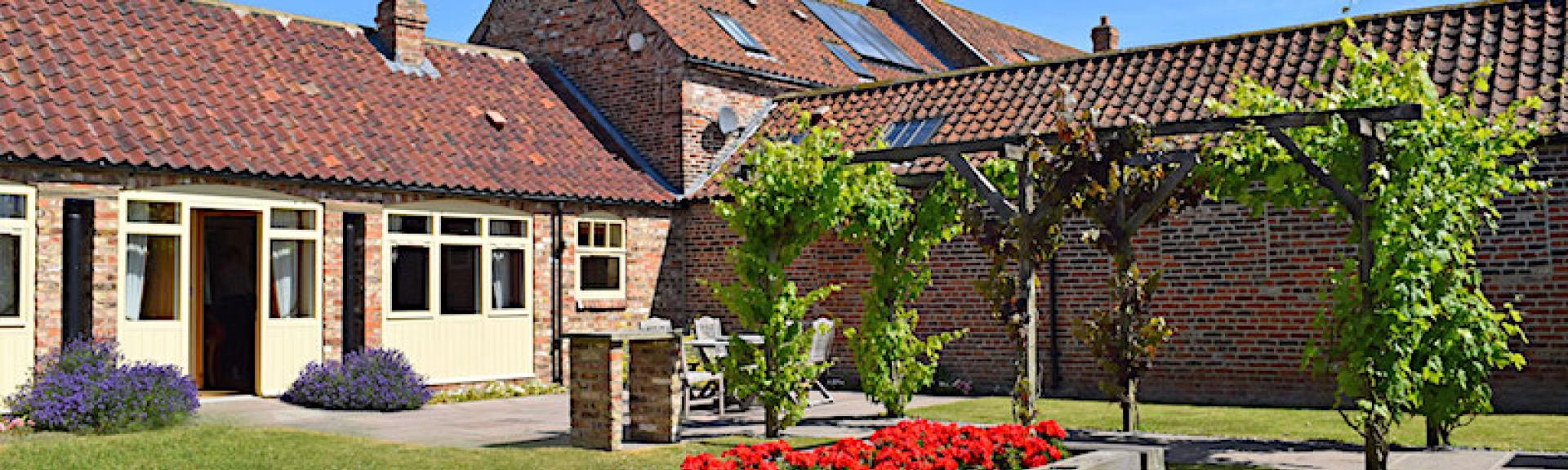 Barn conversion buildings overlooking a grass courtyard with a raised flower bed.