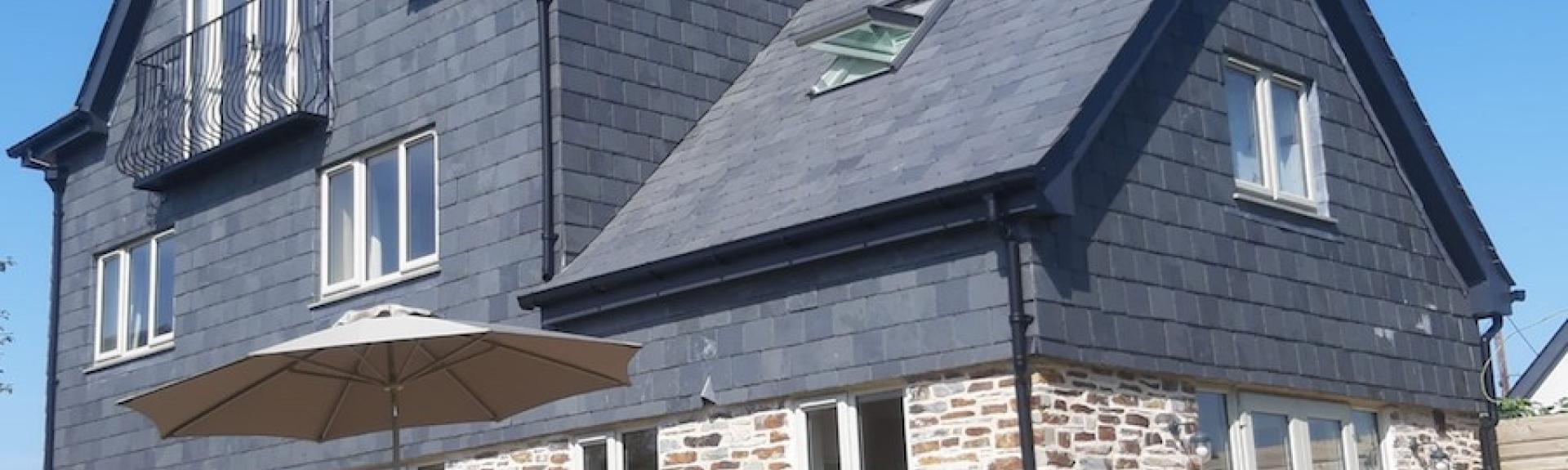 A large, 3-storey detached house built of stone with a 1st floor clad in slates.