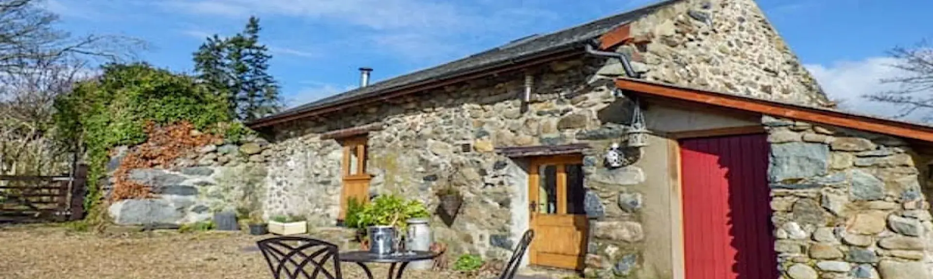 Exterior of a stone built barn conversion overlooking a  courtyard with dining table and chairs.