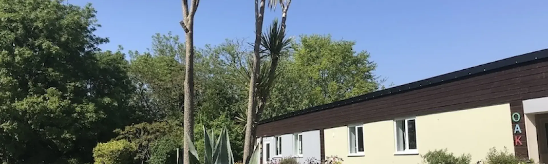 Exterior of a holiday bungalow with a front garden full of shrubs and palm trees.