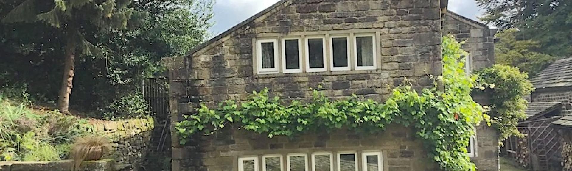 Wisteria-clad, gable end of a restored weavers cottage with two rows of windows in The Pennines.