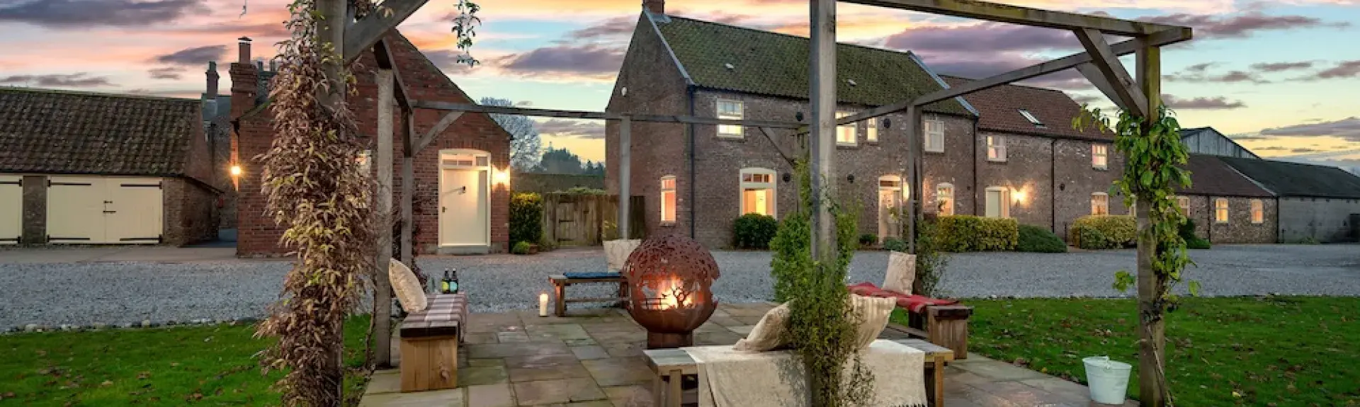 Exterior of a farm cottage and patio with a firepit at sunset.