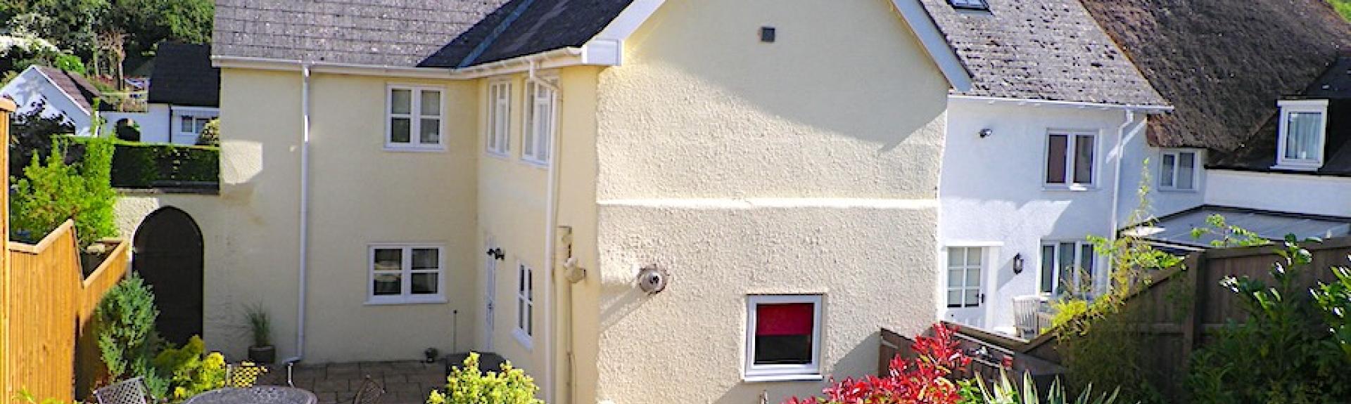 Exterior of a Devon village cottage with a patio and a well-kept garden.