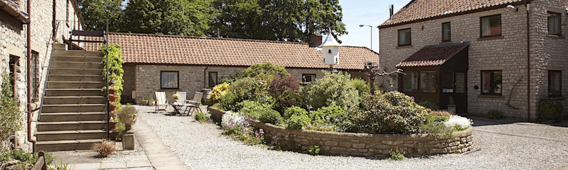 Barn conversions in a courtyard overlook a raised flower bed in its centre