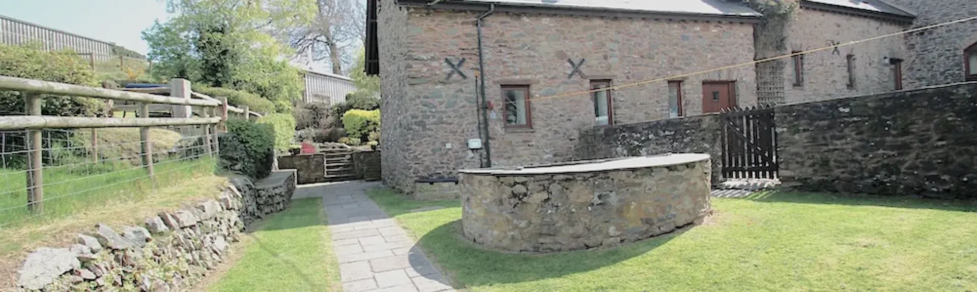 A large Exmoor Farm Cottage overlooks a lawn surrounded by a gated stone wall.