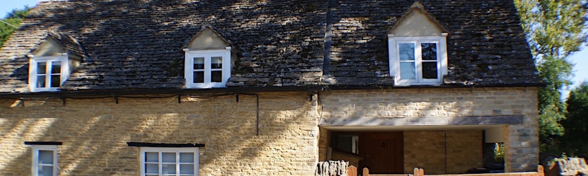 Exterior of a Cotswold stone cottage behind a gated front garden.