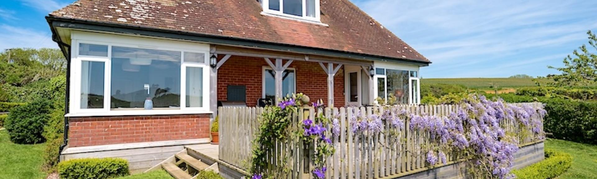 1930s-style detached chalet bungalow with a paved deck surrounded by lawns and the Dorset countryside.