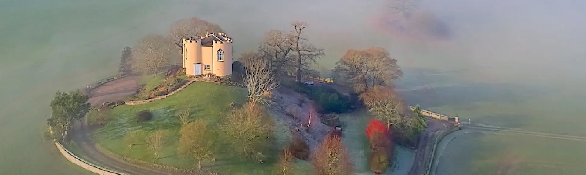 A mock Shropshire castle on a small hillock surrounded by a stone wall and open fields.