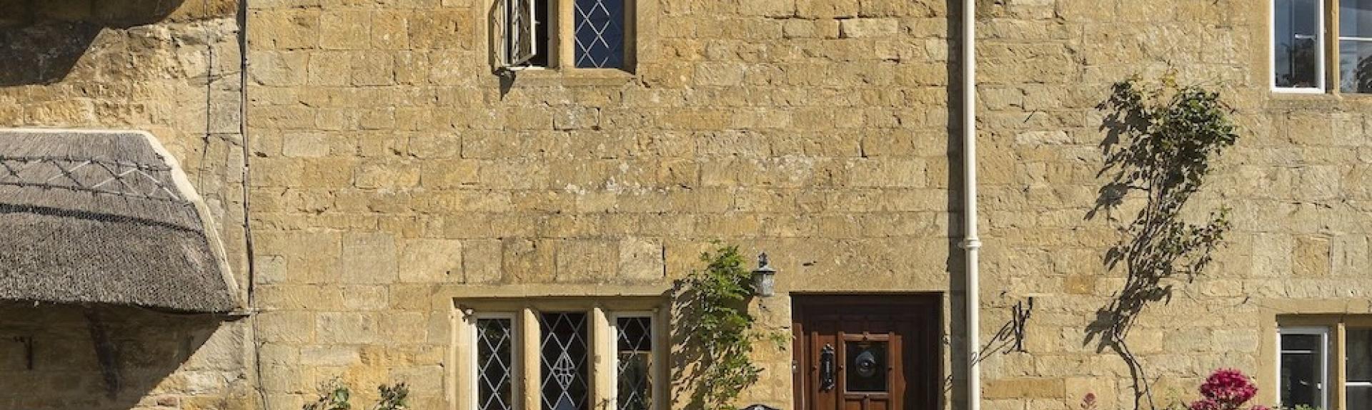 Exterior of a 2-storey, Cotswold 'honey stone' cottage with mullioned windows.