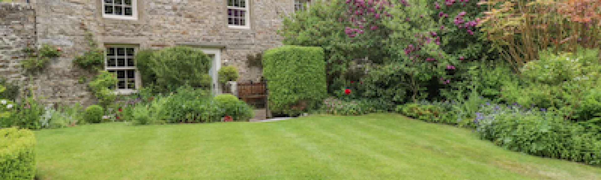 A large stone-built farmhouse overlooks a secure lawn and flower beds.