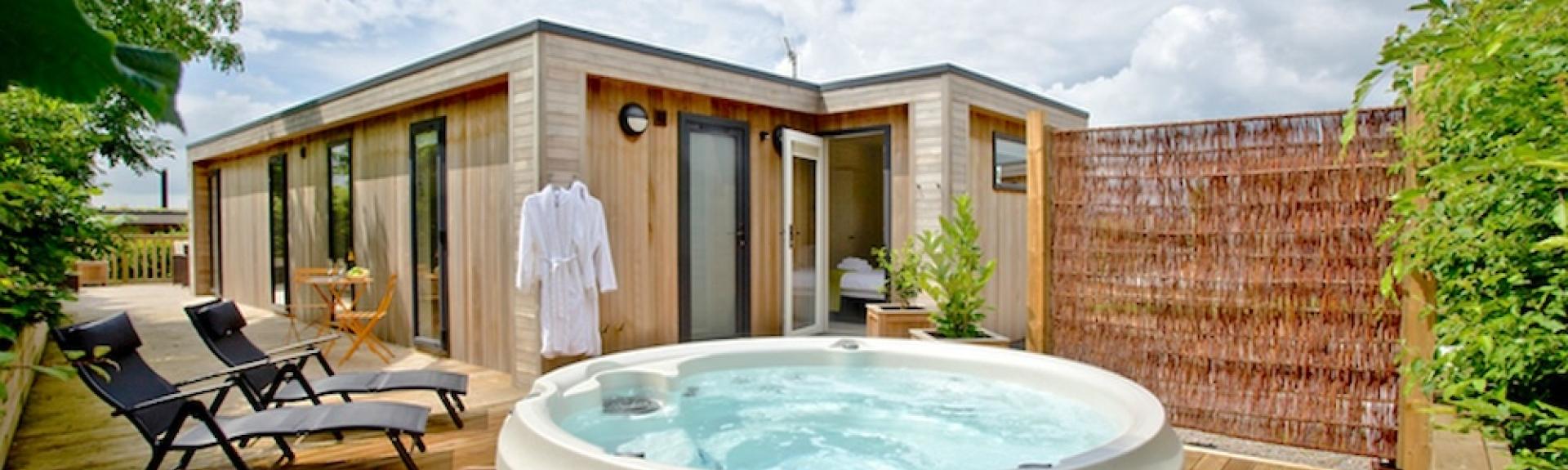 Exterior of a wooden eco lodge with a hot tub on its deck.