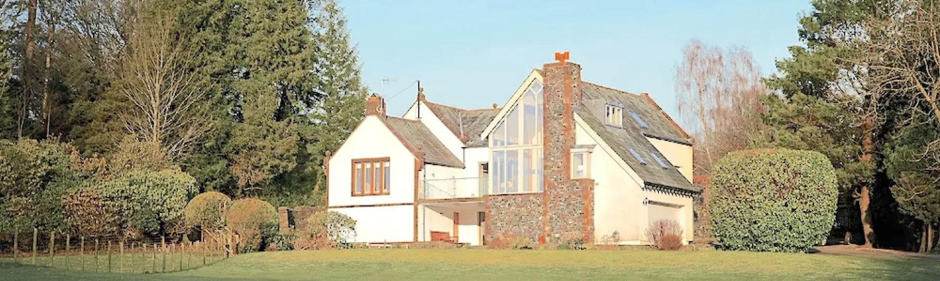 A twin-gabled house overlooks a large lawn bordered by a tall hedge.