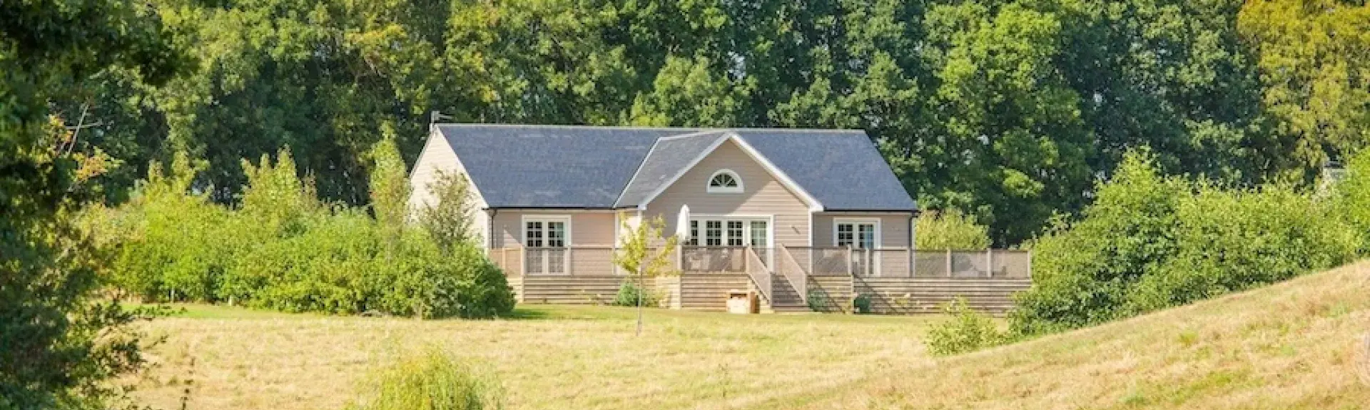 A timbered eco-lodge sits in front of mature woods overlooking open fields.