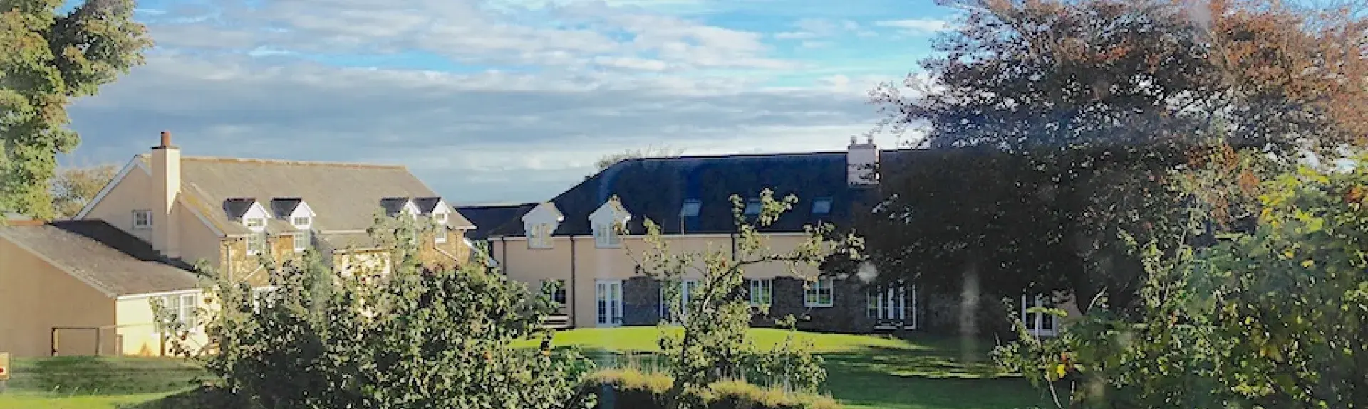 A large lawn with apple trees has a row of farm cottages in the background.