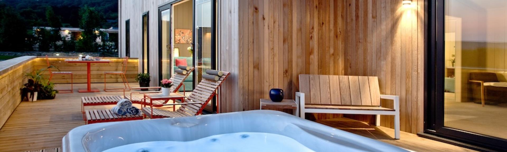 A hot tub and sunloungers on the deck of an timber eco lodge.