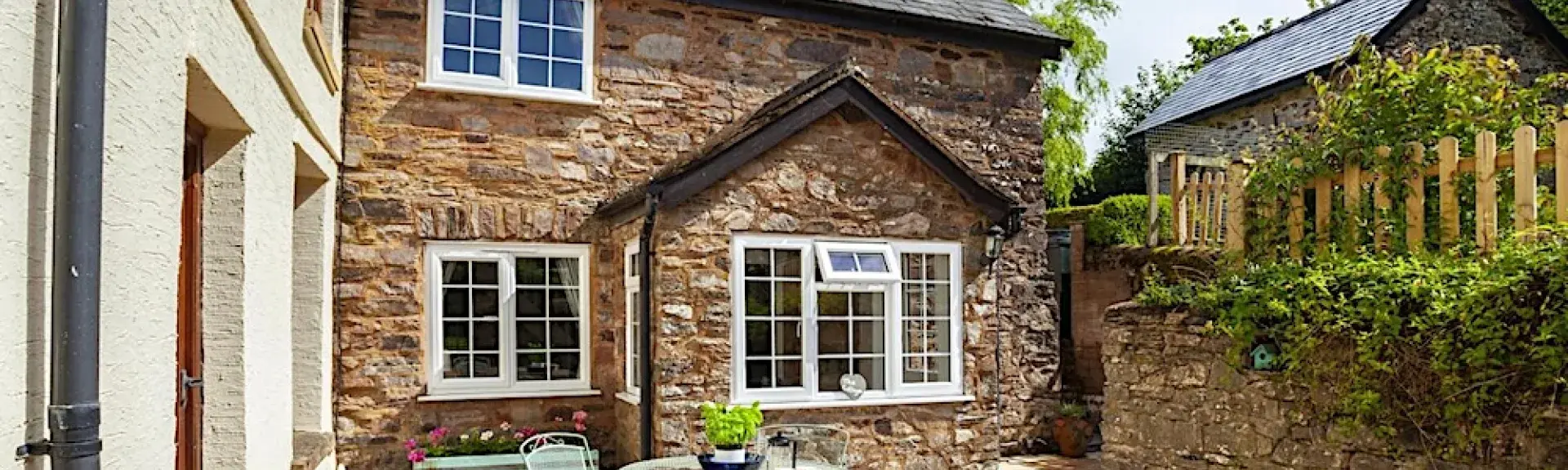 Exterior of a stone-built cottage overlooking a paved courtyard with dining table and chairs.